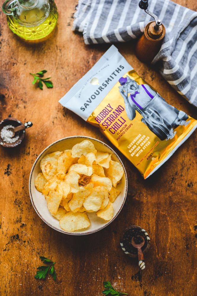 Savoursmiths Bubbly Serrano Chilli crisps pack beside a filled bowl on a wooden table